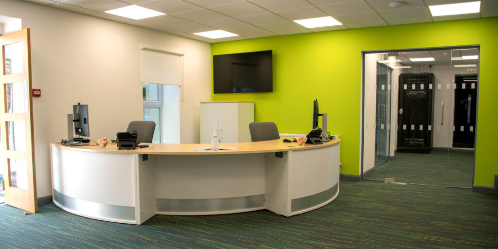 Reception at Kingdom House. Curved front desk with green wall and a large screen.