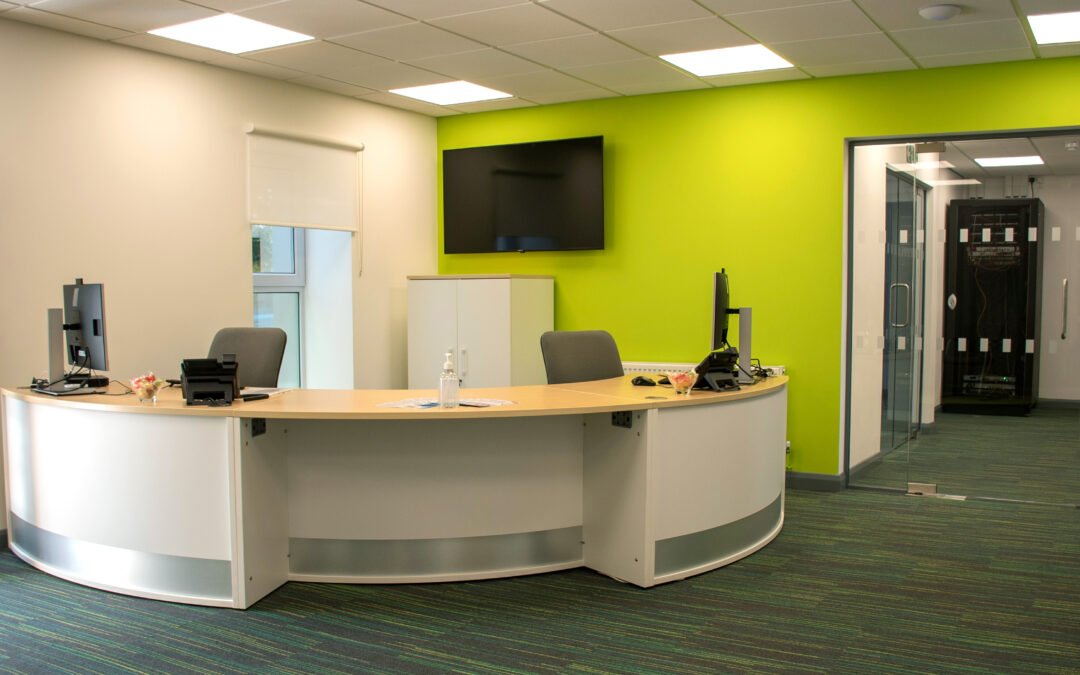 Reception at Kingdom House. Curved front desk with green wall and a large screen.
